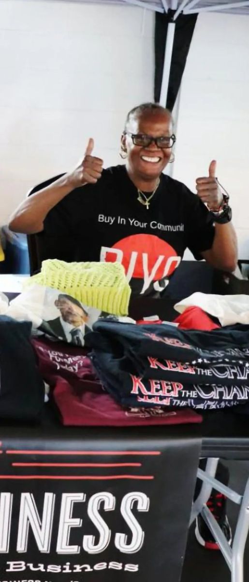 A smiling vendor with two thumbs up in a Buy In Your Community shirt